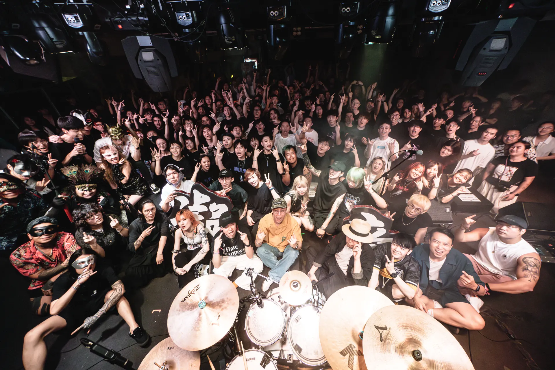 緊急祭現場大合照:樂手與觀眾在香港 live house 合影,前景有鼓組,有人舉起緊急祭字牌。